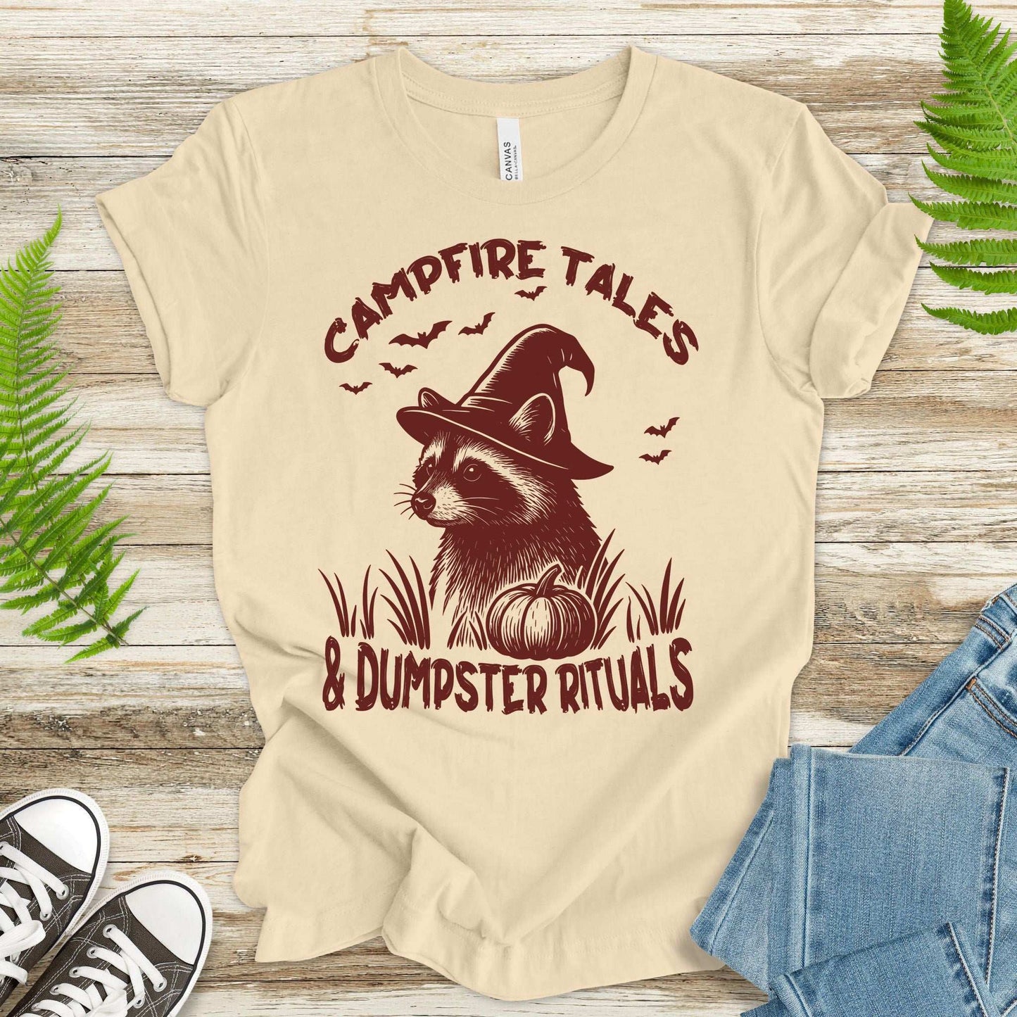 Campfire Tales Raccoon Halloween T-shirt featuring a witchy raccoon and pumpkin design for festive spooky vibes.