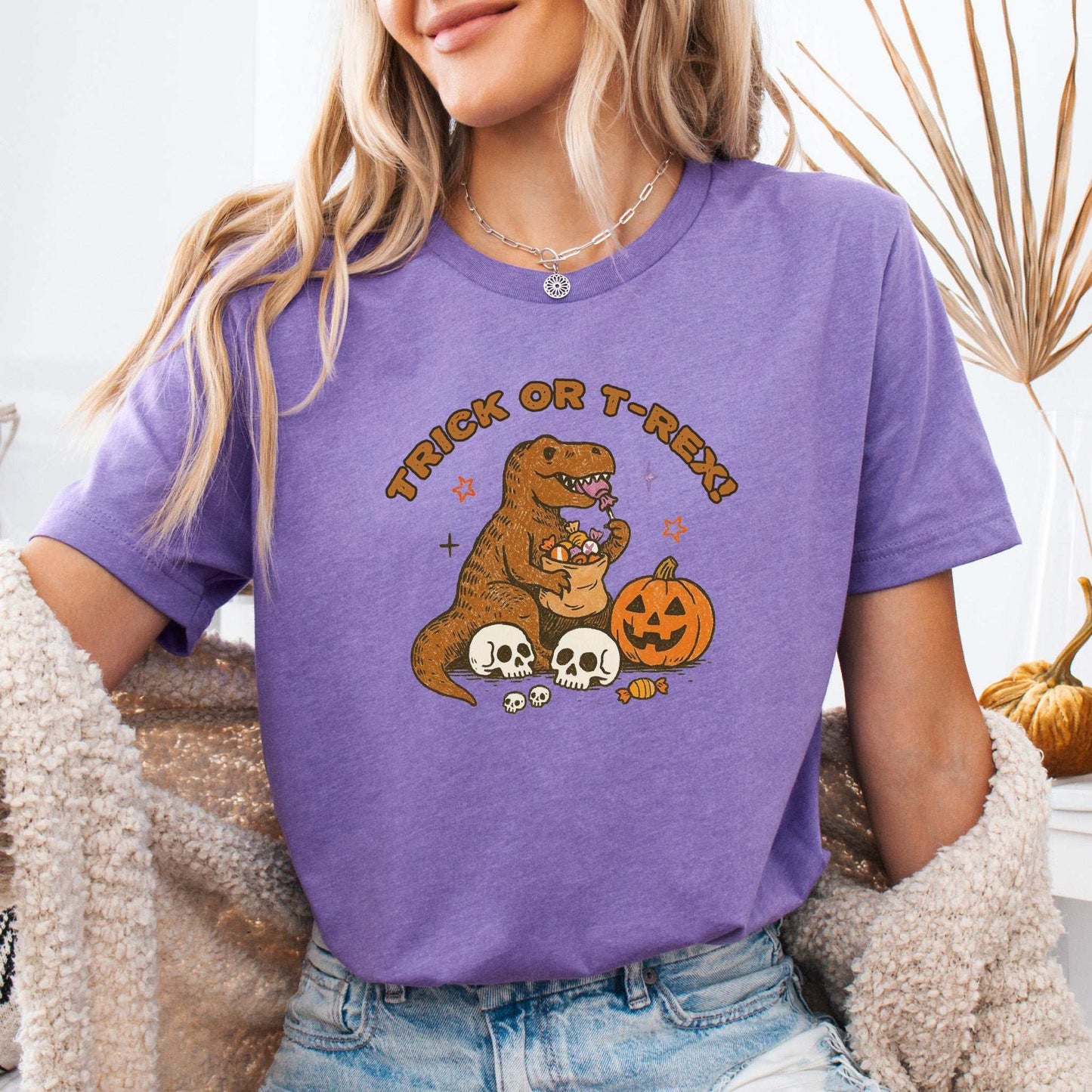 T-Rex Halloween T-Shirt featuring a dinosaur with candy, skeletons, and a pumpkin, perfect for Trick or Treat vibes.