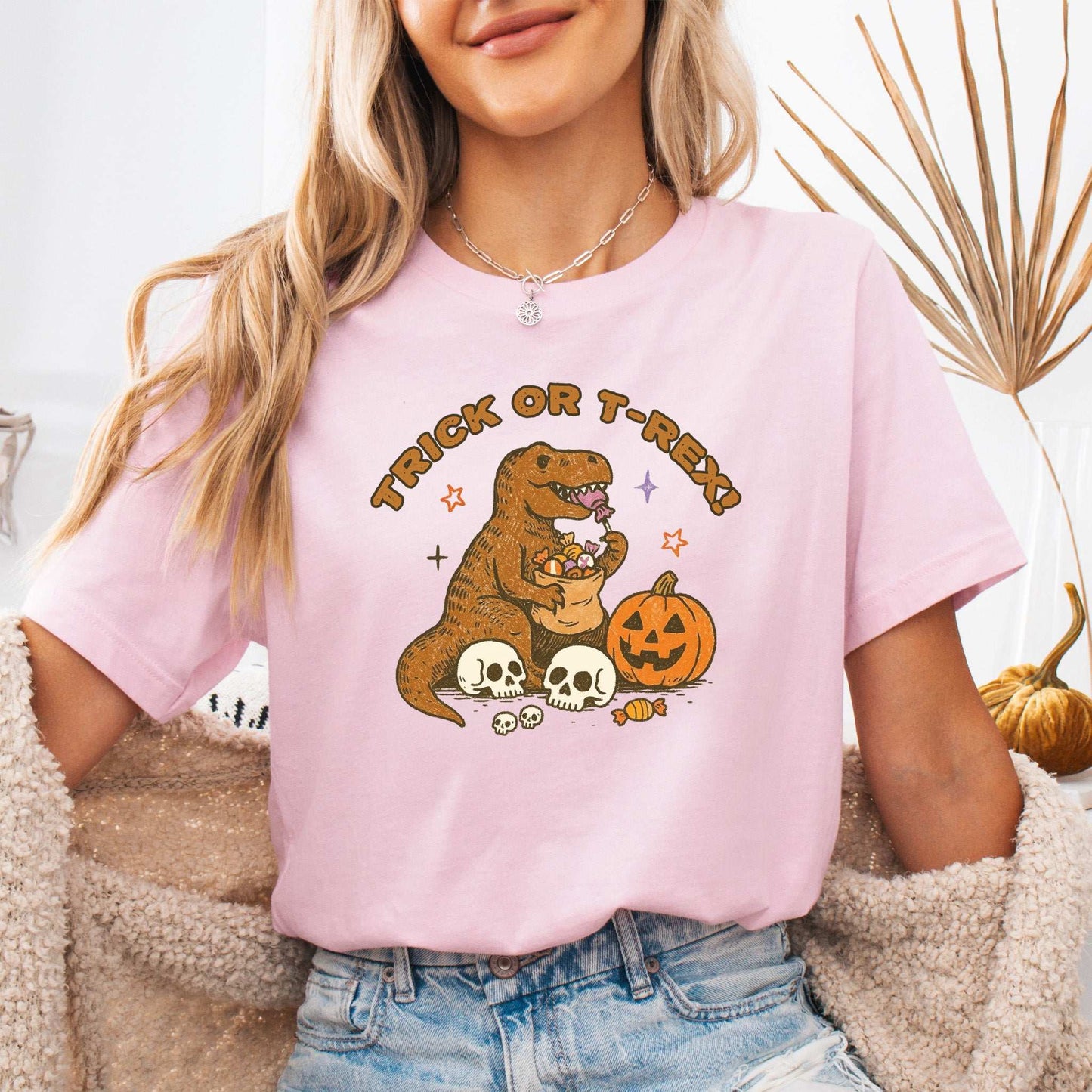 Trick or T-Rex Halloween T-Shirt featuring a dino with candy, skulls, and a pumpkin in a fun design.