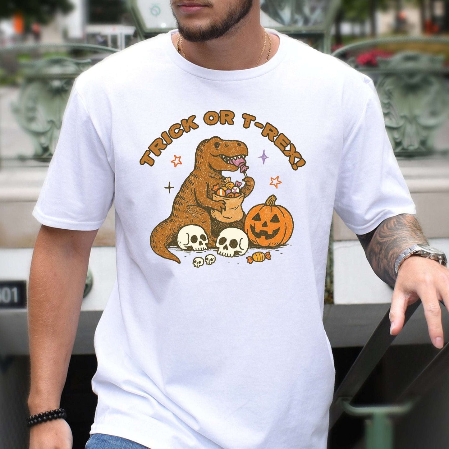 T-Rex Halloween T-Shirt featuring a dino with candy, skulls, and a pumpkin, perfect for Trick or Treat enthusiasts.