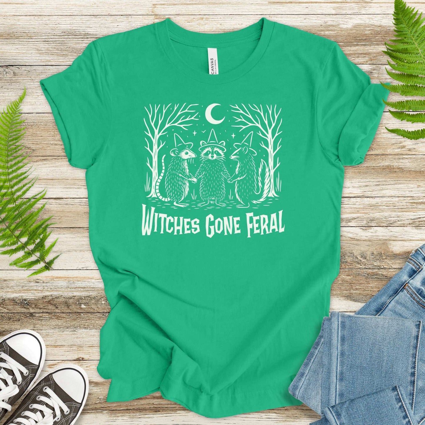 Witches Gone Feral Halloween T-shirt featuring a raccoon, opossum, and skunk under a crescent moon in a forest.