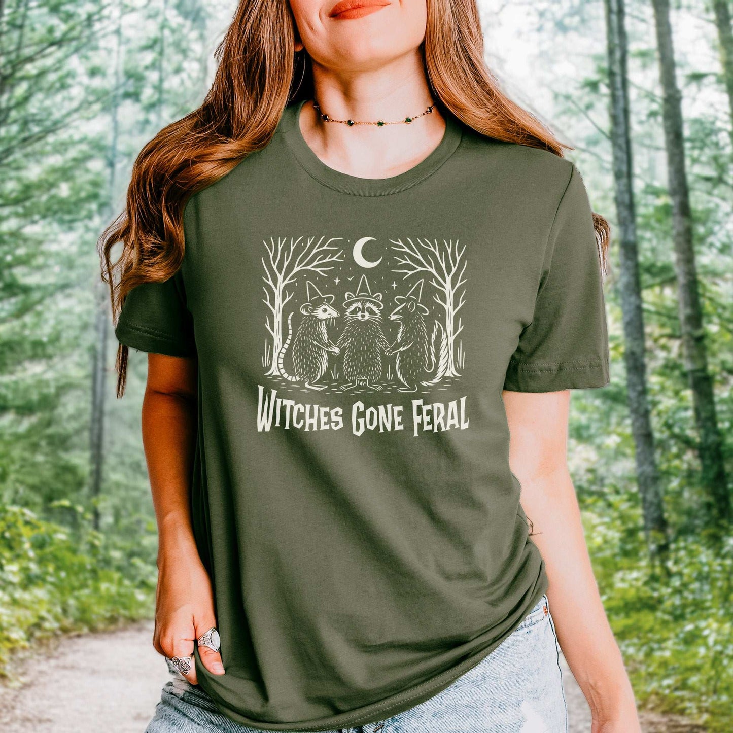 Witches Gone Feral Halloween T-shirt featuring raccoon, opossum, and skunk in a magical forest setting.