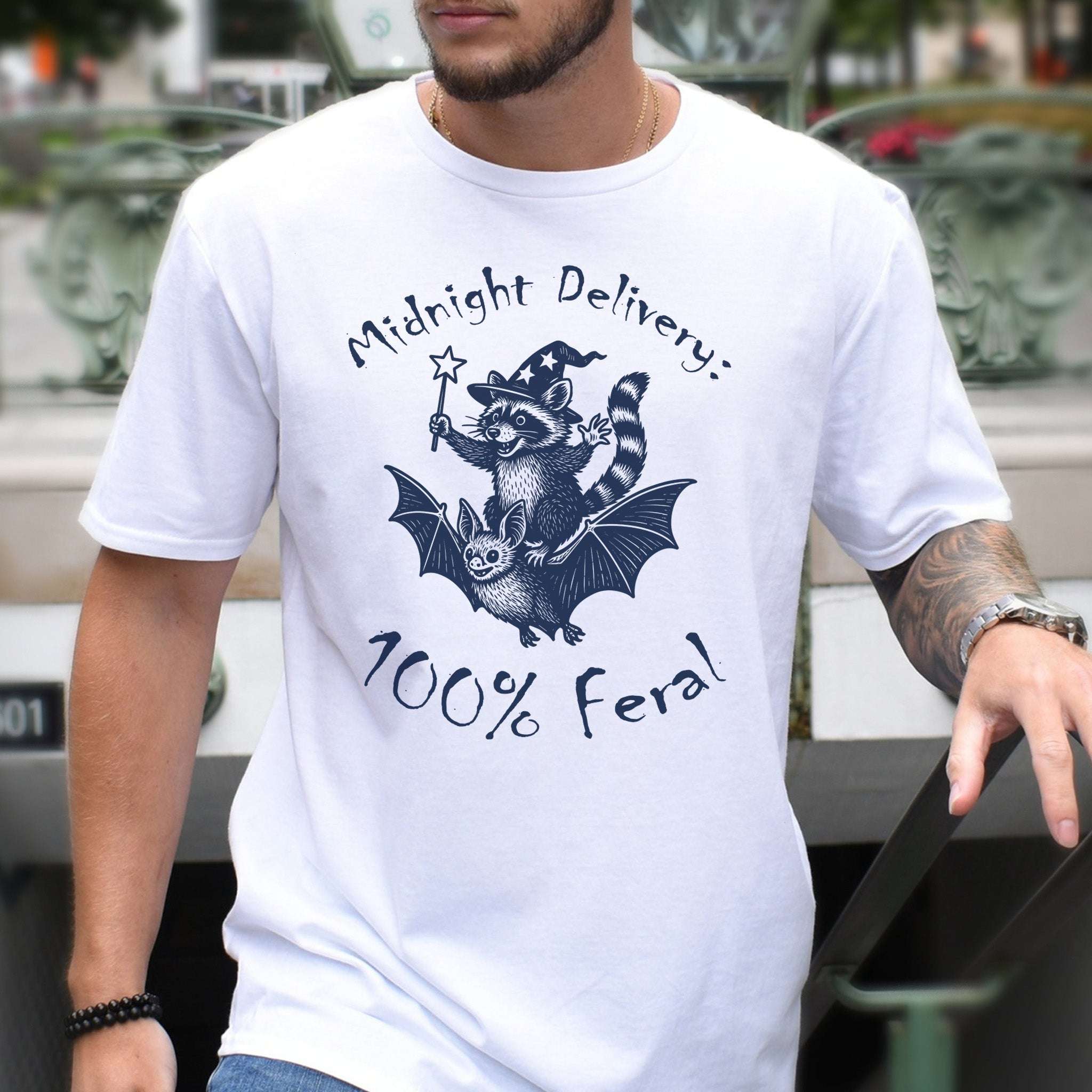 Midnight Delivery Raccoon Halloween T-shirt featuring a wizard raccoon riding a bat, playful and magical design.