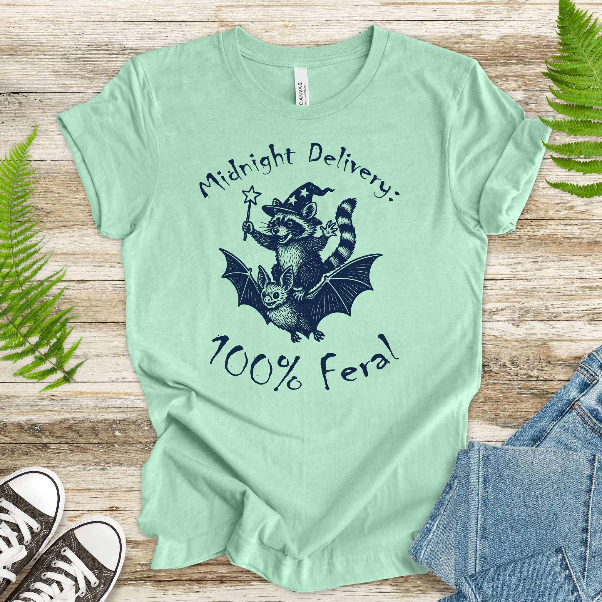 Midnight Delivery Raccoon Halloween T-Shirt featuring a whimsical design of a raccoon riding a bat, 100% feral style.