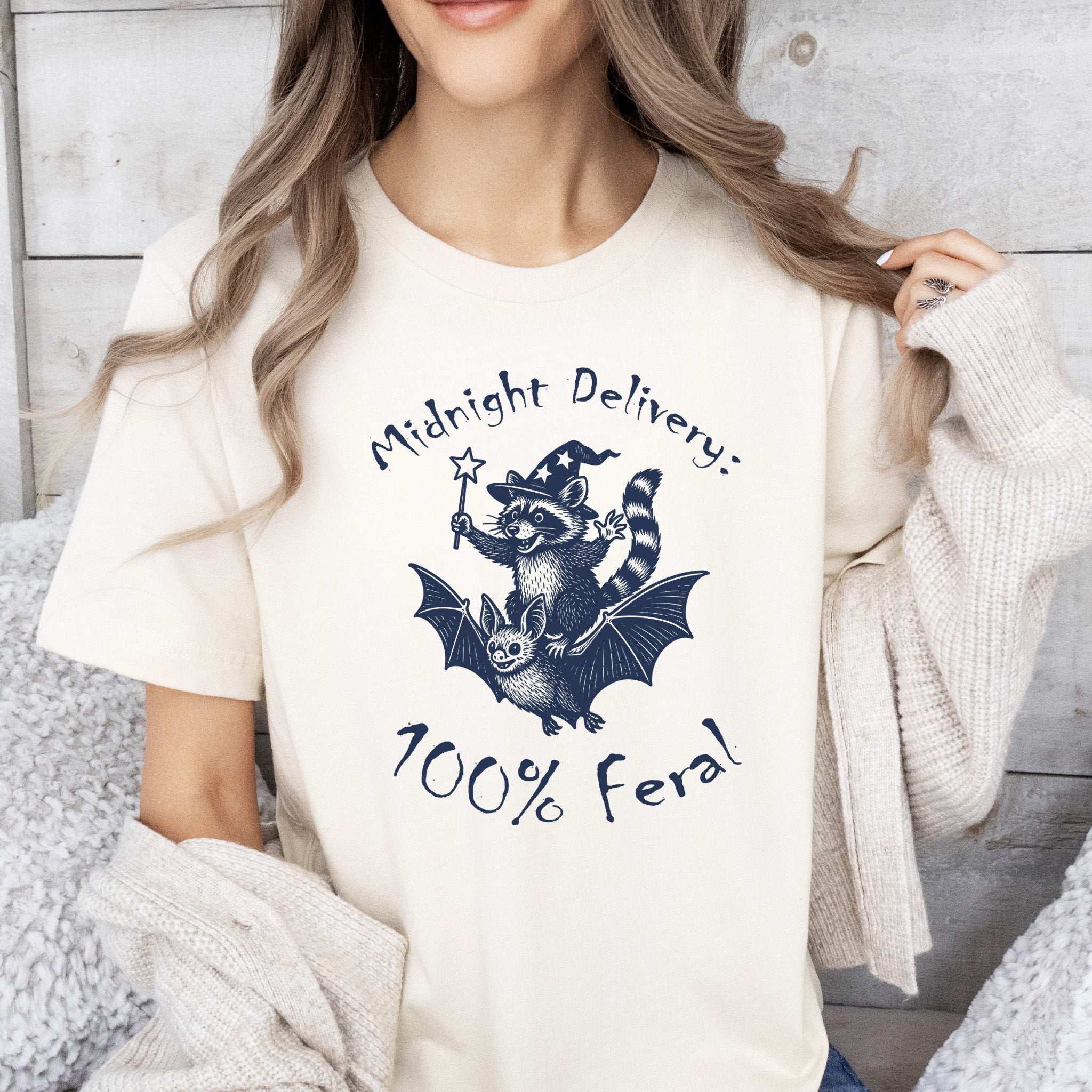 Midnight Delivery Raccoon Halloween T-shirt with 100% Feral design featuring a raccoon riding a bat.