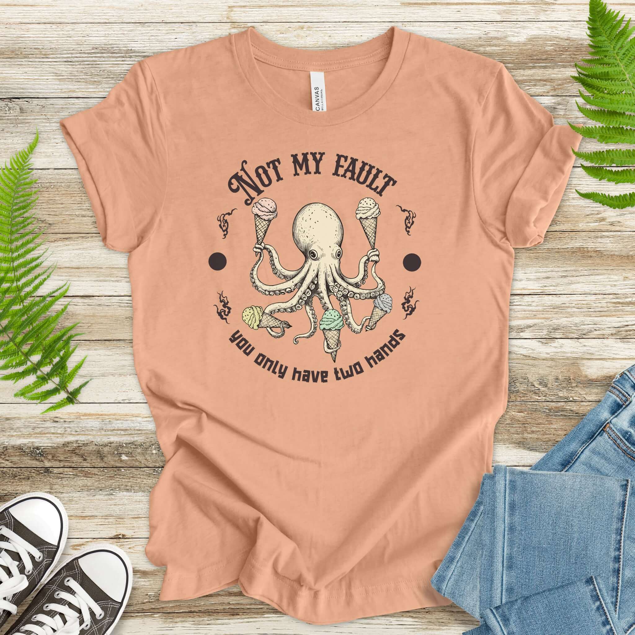 Funny octopus ice cream lover T-shirt with text 'Not My Fault, You Only Have Two Hands' on a soft peach background.