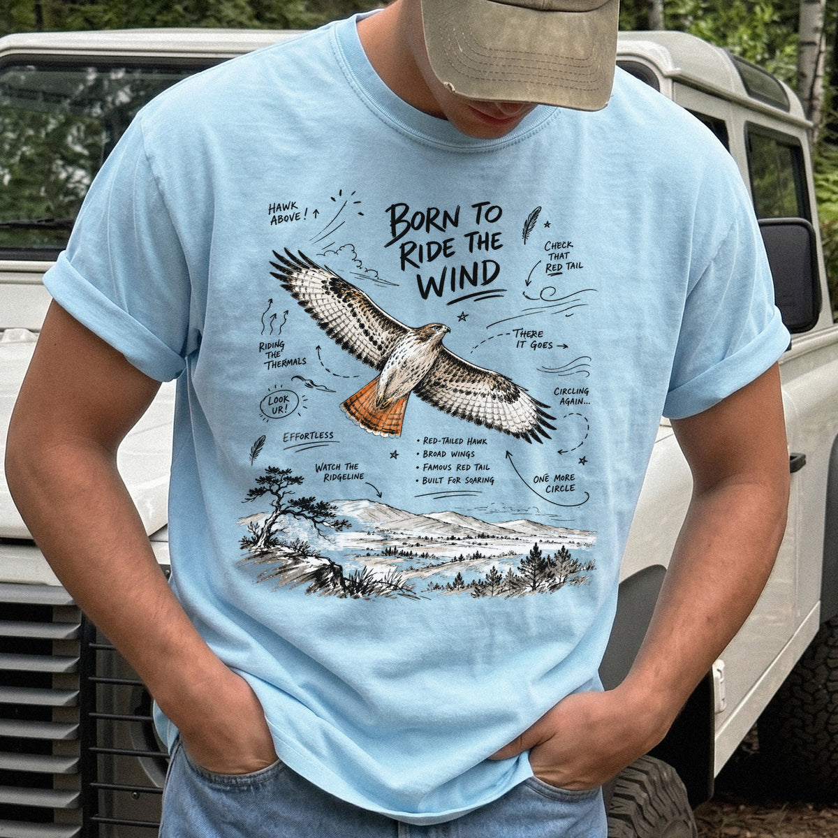 Born to Ride the Wind Comfort Colors Shirt – Red-Tailed Hawk design of a Red-Tailed Hawk illustrated in flight above an open ridgeline, with field-note style callouts and a scenic landscape below, printed on a Chambray T-shirt.