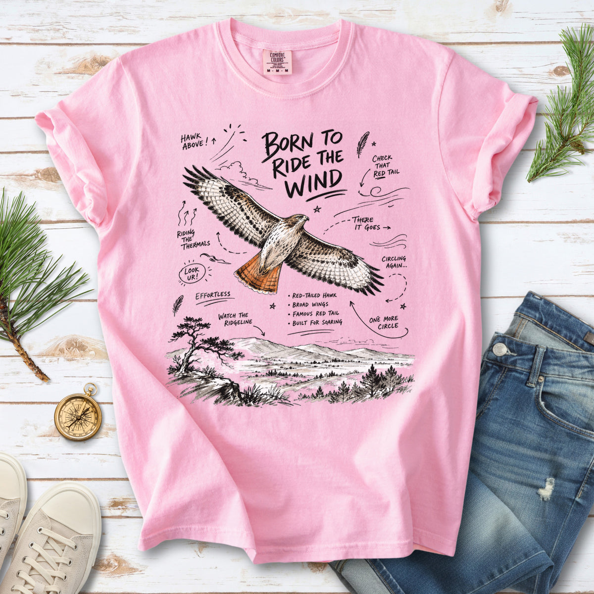 Born to Ride the Wind Comfort Colors Shirt – Red-Tailed Hawk design of a Red-Tailed Hawk illustrated in flight above an open ridgeline, with field-note style callouts and a scenic landscape below, printed on a Blossom T-shirt.