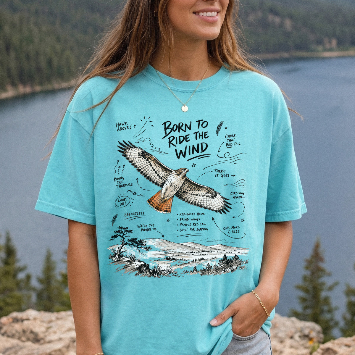 Born to Ride the Wind Comfort Colors Shirt – Red-Tailed Hawk design of a Red-Tailed Hawk illustrated in flight above an open ridgeline, with field-note style callouts and a scenic landscape below, printed on a Chalky Mint T-shirt, worn by a woman.