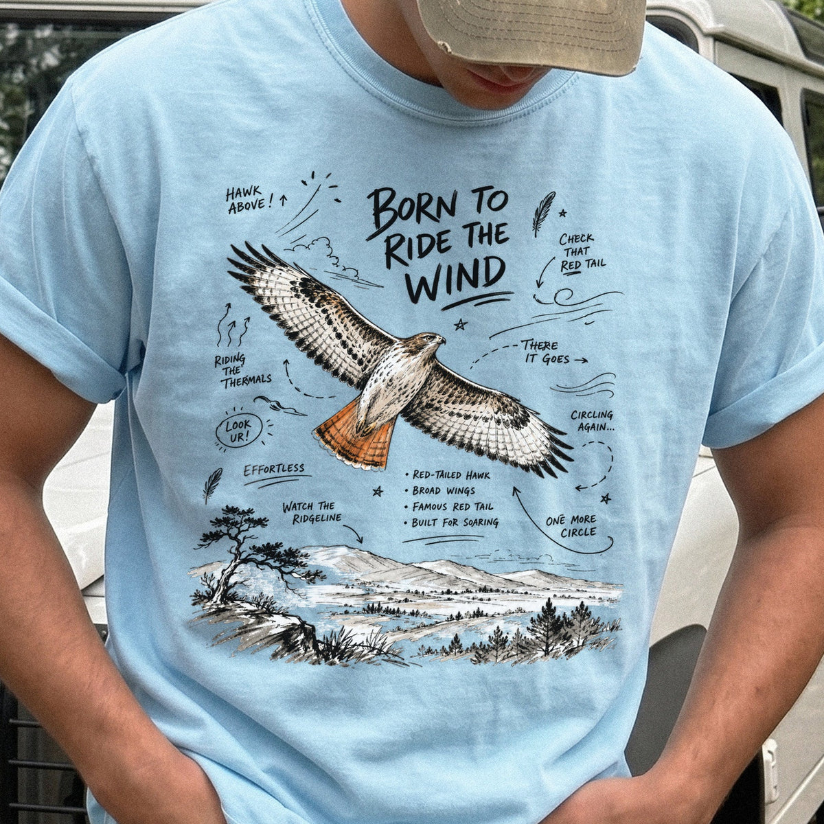 Born to Ride the Wind Comfort Colors Shirt – Red-Tailed Hawk design of a Red-Tailed Hawk illustrated in flight above an open ridgeline, with field-note style callouts and a scenic landscape below, printed on a Chambray T-shirt.