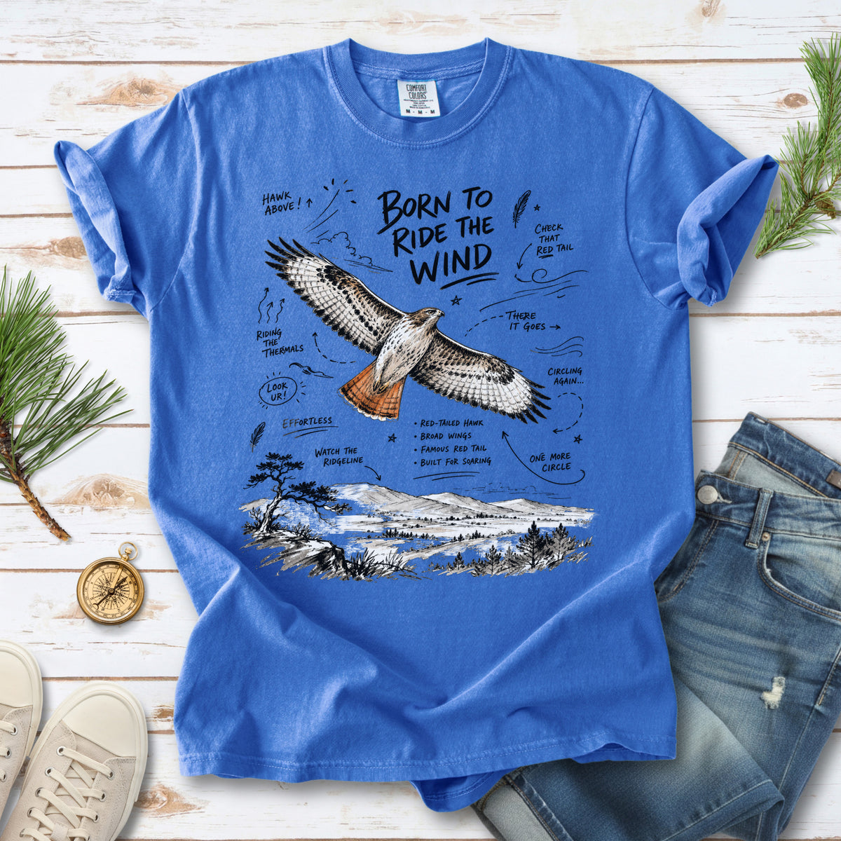 Born to Ride the Wind Comfort Colors Shirt – Red-Tailed Hawk design of a Red-Tailed Hawk illustrated in flight above an open ridgeline, with field-note style callouts and a scenic landscape below, printed on a Flo Blue T-shirt.