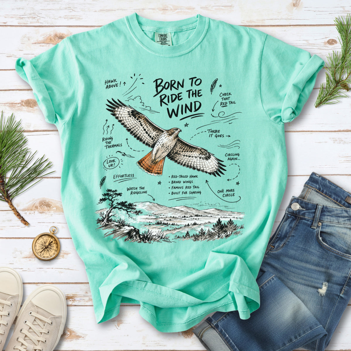 Born to Ride the Wind Comfort Colors Shirt – Red-Tailed Hawk design of a Red-Tailed Hawk illustrated in flight above an open ridgeline, with field-note style callouts and a scenic landscape below, printed on an Island Reef T-shirt.