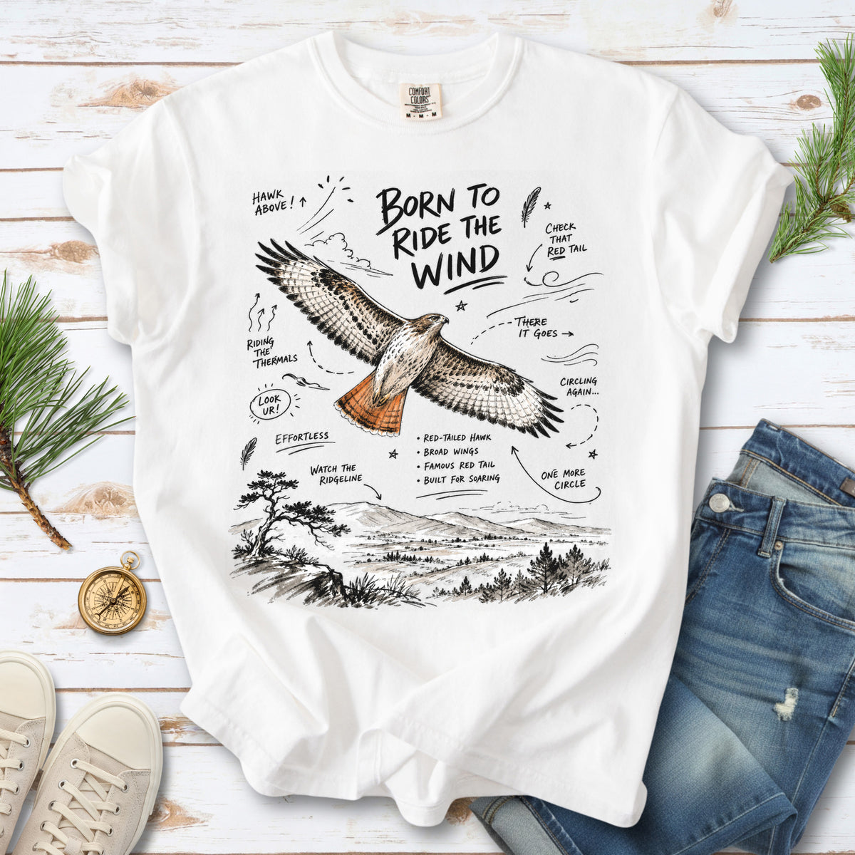 Born to Ride the Wind Comfort Colors Shirt – Red-Tailed Hawk design of a Red-Tailed Hawk illustrated in flight above an open ridgeline, with field-note style callouts and a scenic landscape below, printed on a White T-shirt.
