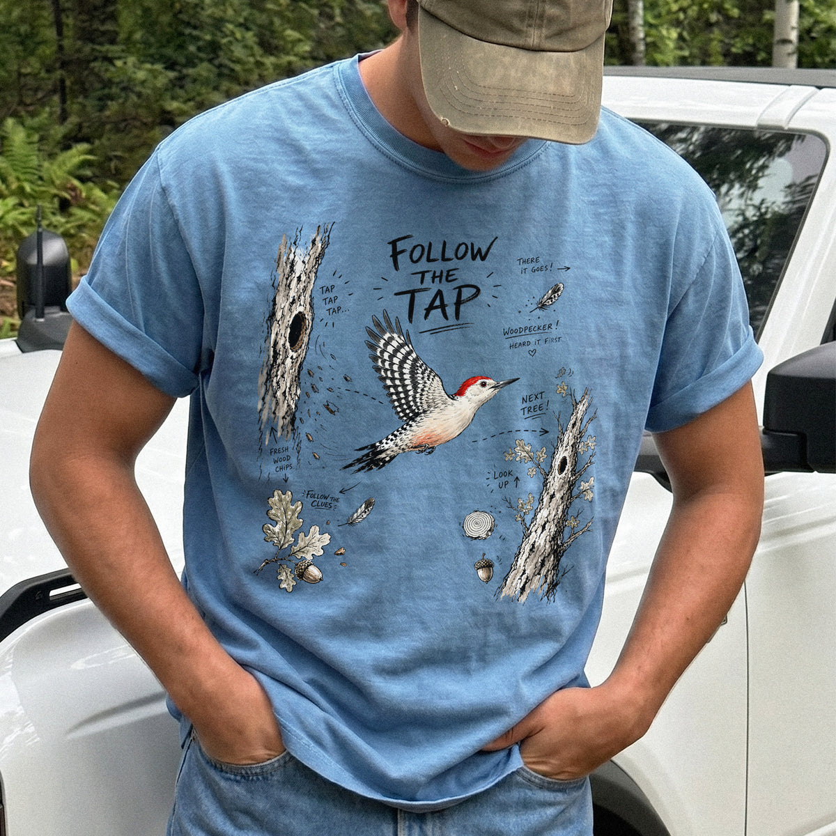 Follow the Tap Comfort Colors Shirt – Red-Bellied Woodpecker design of a Red-Bellied Woodpecker illustrated in flight, surrounded by tree trunks, wood chips, feathers, oak leaves, and acorn details, printed on a Blue Jean T-shirt.