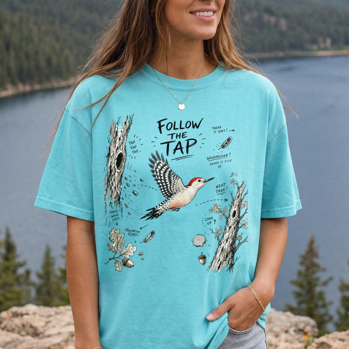 Follow the Tap Comfort Colors Shirt – Red-Bellied Woodpecker design of a Red-Bellied Woodpecker illustrated in flight, surrounded by tree trunks, wood chips, feathers, oak leaves, and acorn details, printed on a Chalky Mint T-shirt, worn by a woman.