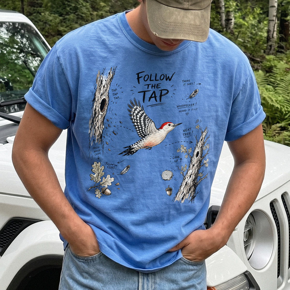 Follow the Tap Comfort Colors Shirt – Red-Bellied Woodpecker design of a Red-Bellied Woodpecker illustrated in flight, surrounded by tree trunks, wood chips, feathers, oak leaves, and acorn details, printed on a Flo Blue T-shirt.