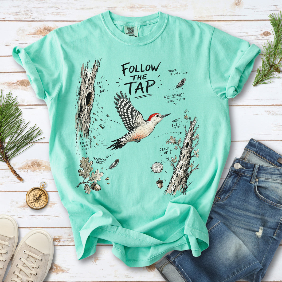 Follow the Tap Comfort Colors Shirt – Red-Bellied Woodpecker design of a Red-Bellied Woodpecker illustrated in flight, surrounded by tree trunks, wood chips, feathers, oak leaves, and acorn details, printed on an Island Reef T-shirt.