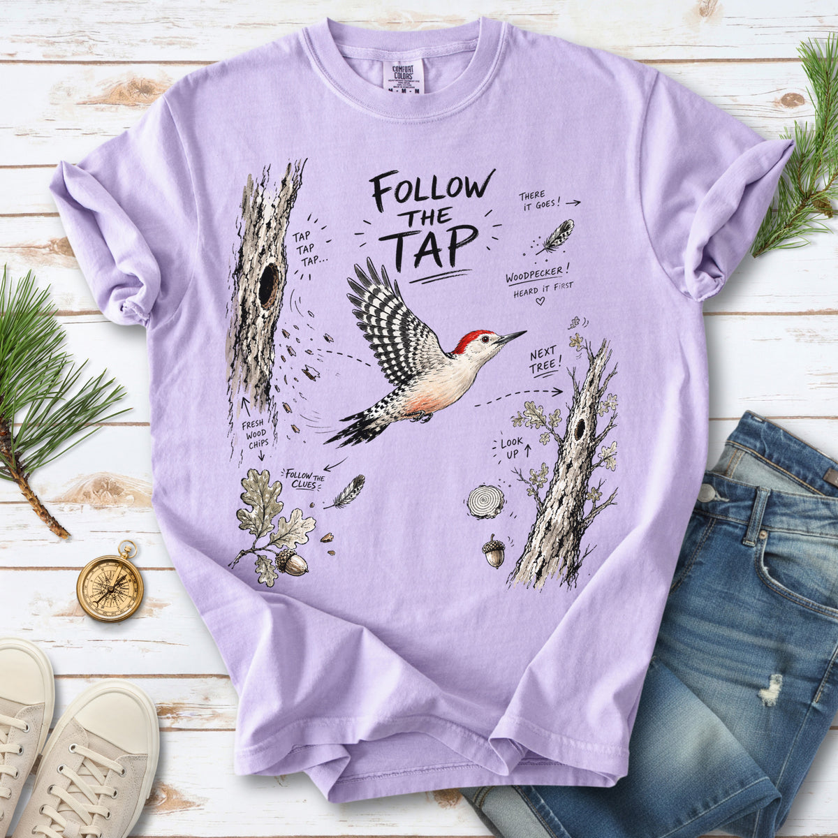 Follow the Tap Comfort Colors Shirt – Red-Bellied Woodpecker design of a Red-Bellied Woodpecker illustrated in flight, surrounded by tree trunks, wood chips, feathers, oak leaves, and acorn details, printed on an Orchid T-shirt.