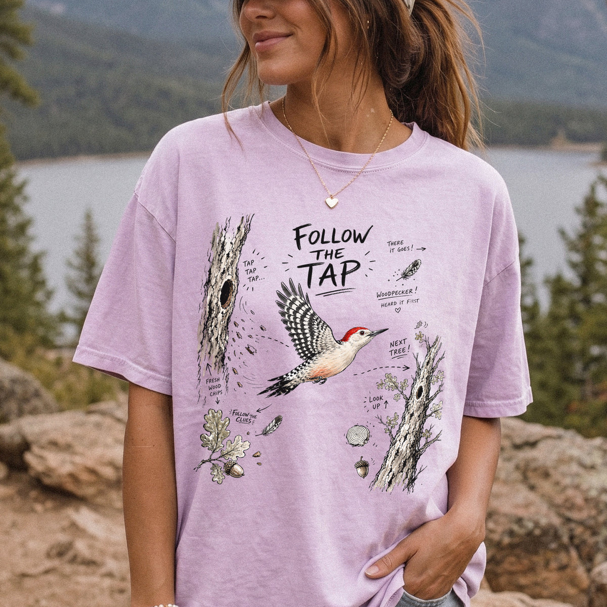 Follow the Tap Comfort Colors Shirt – Red-Bellied Woodpecker design of a Red-Bellied Woodpecker illustrated in flight, surrounded by tree trunks, wood chips, feathers, oak leaves, and acorn details, printed on an Orchid T-shirt, worn by a woman.