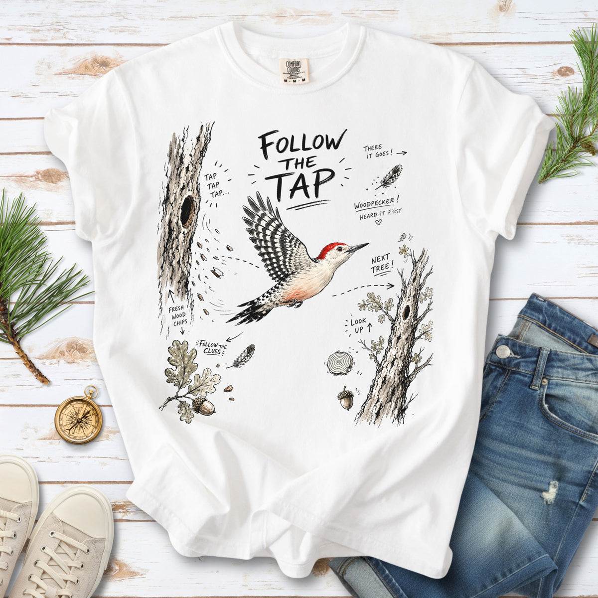 Follow the Tap Comfort Colors Shirt – Red-Bellied Woodpecker design of a Red-Bellied Woodpecker illustrated in flight, surrounded by tree trunks, wood chips, feathers, oak leaves, and acorn details, printed on a White T-shirt.