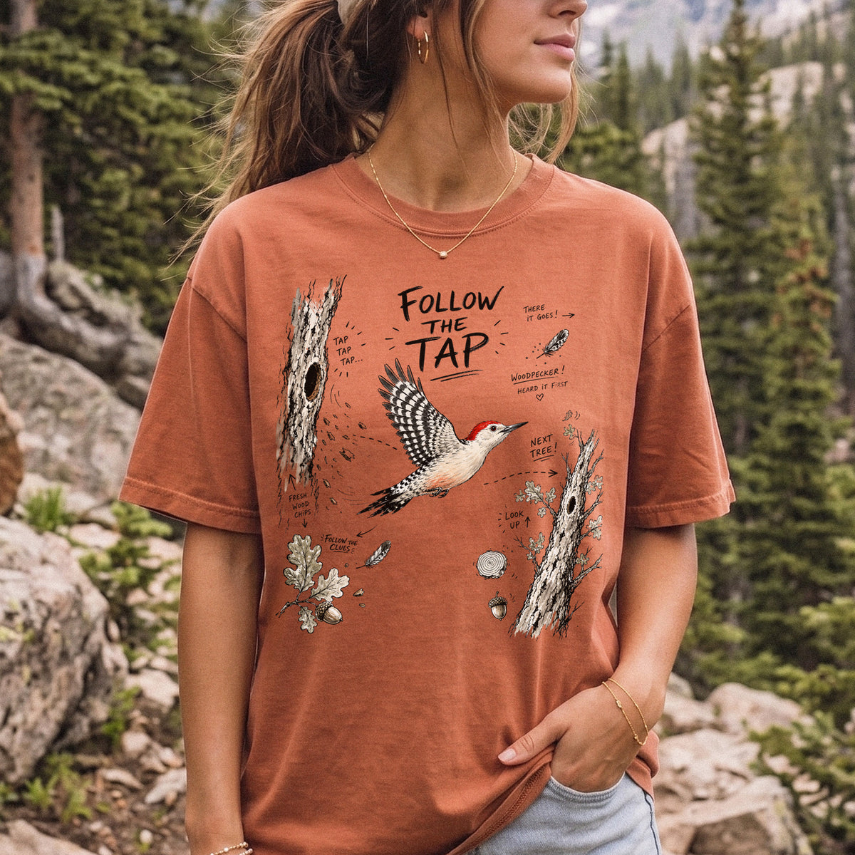 Follow the Tap Comfort Colors Shirt – Red-Bellied Woodpecker design of a Red-Bellied Woodpecker illustrated in flight, surrounded by tree trunks, wood chips, feathers, oak leaves, and acorn details, printed on a Yam T-shirt, worn by a woman.