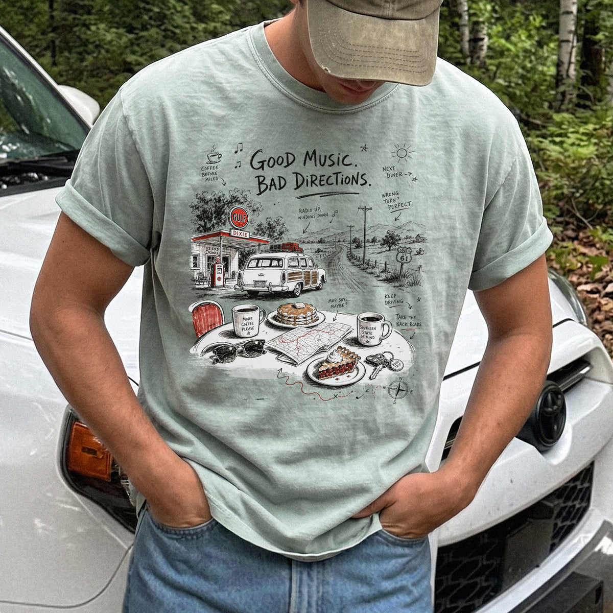 Man wearing a Bay Comfort Colors T-shirt with a vintage roadside scene with a classic car, old gas station, and a winding back road