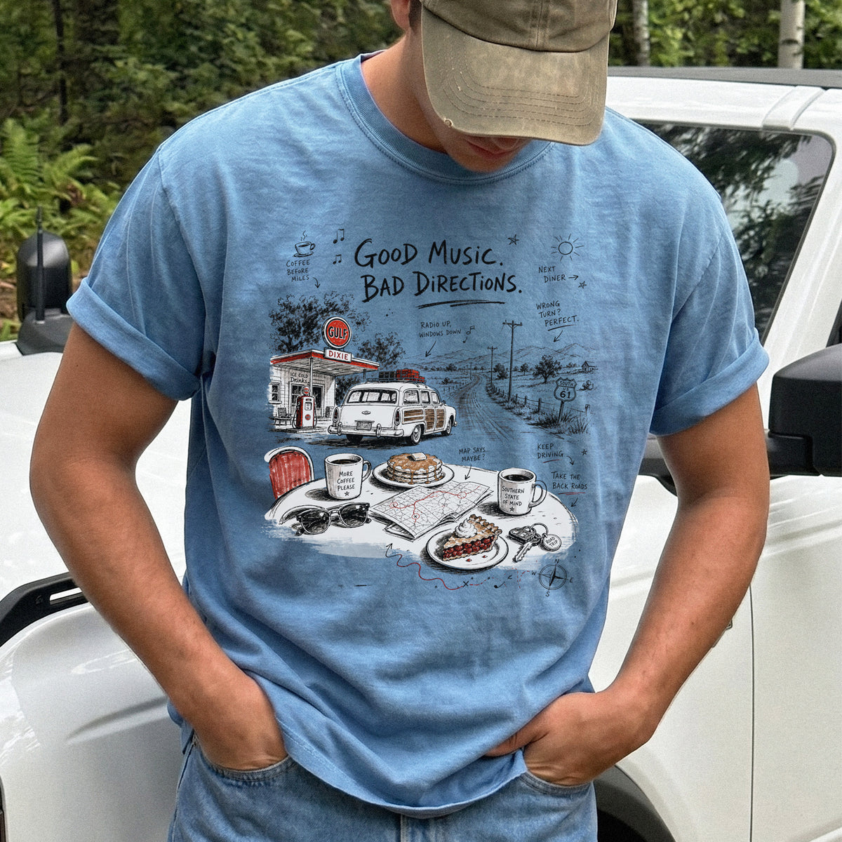 Man wearing a Blue Jean Comfort Colors T-shirt with a vintage roadside scene with a classic car, old gas station, and a winding back road