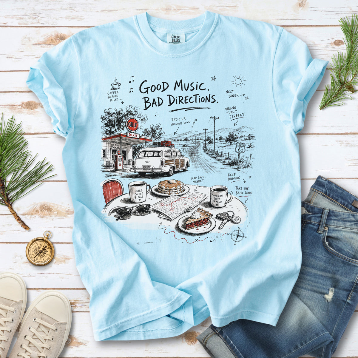 A vintage roadside scene with a classic car, old gas station, and a winding back road design on a Chambray Comfort Colors T-shirt