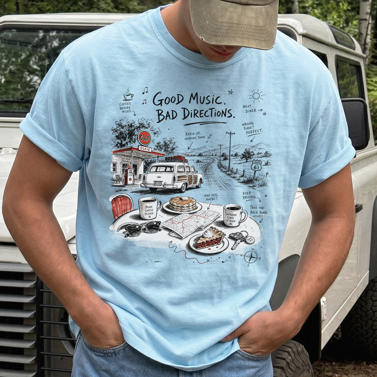 Man wearing a Chambray Comfort Colors T-shirt with a vintage roadside scene with a classic car, old gas station, and a winding back road