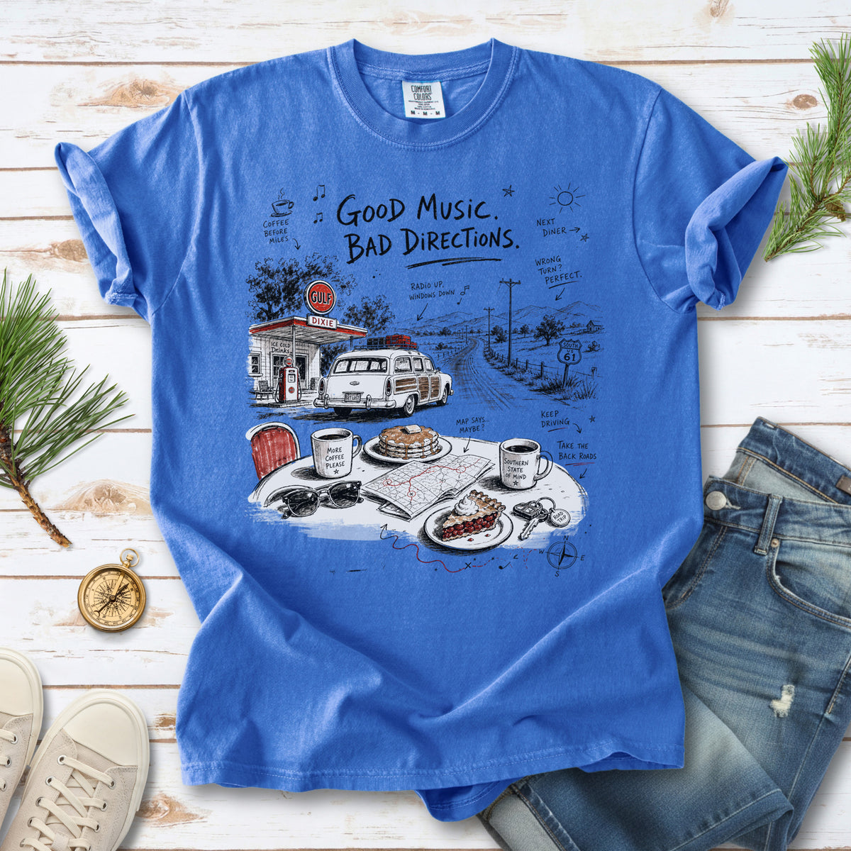 A vintage roadside scene with a classic car, old gas station, and a winding back road design on a Flo Blue Comfort Colors T-shirt