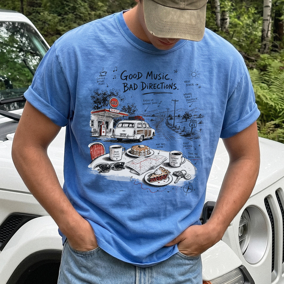 Man wearing a Flo Blue Comfort Colors T-shirt with a vintage roadside scene with a classic car, old gas station, and a winding back road