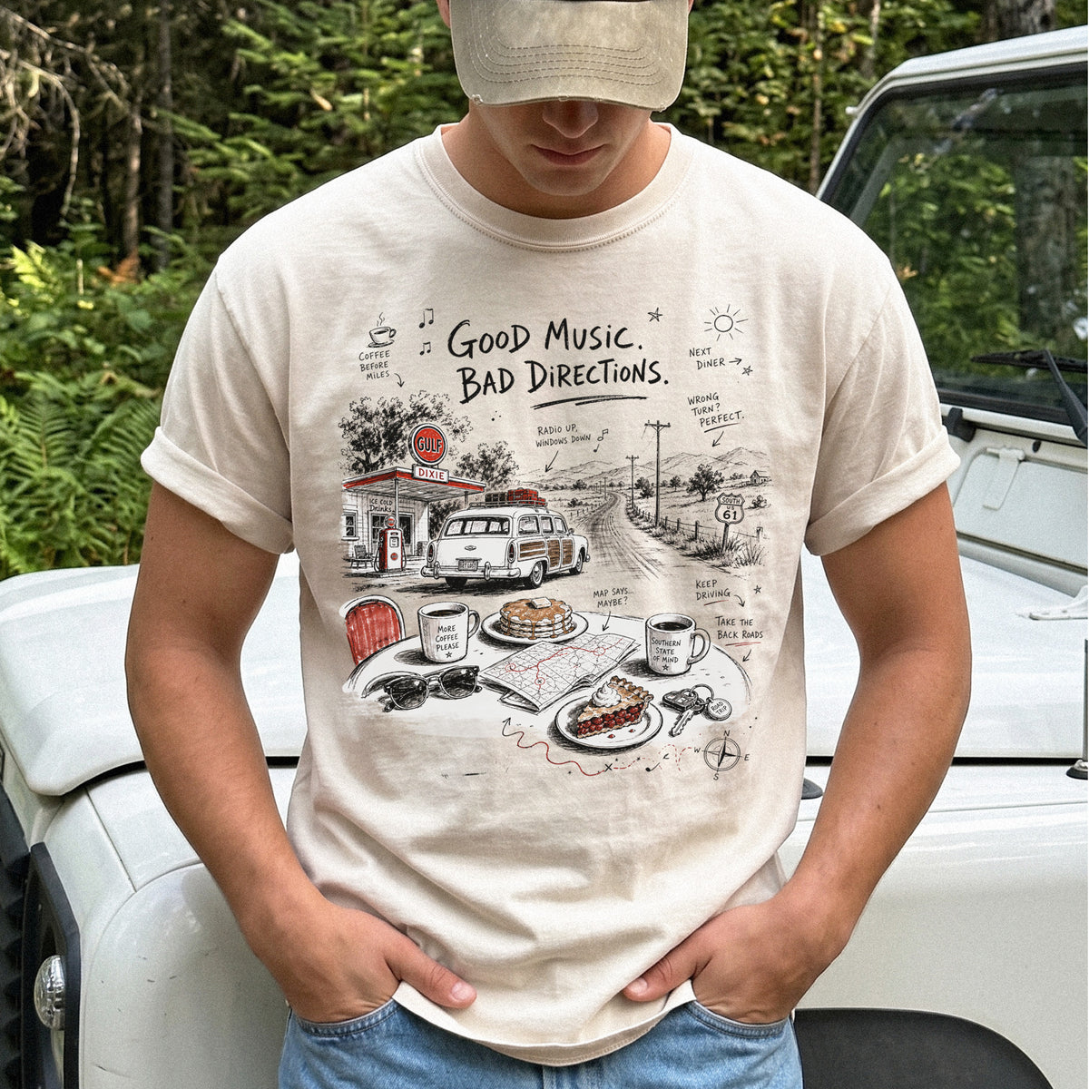 Man wearing an Ivory Comfort Colors T-shirt with a vintage roadside scene with a classic car, old gas station, and a winding back road