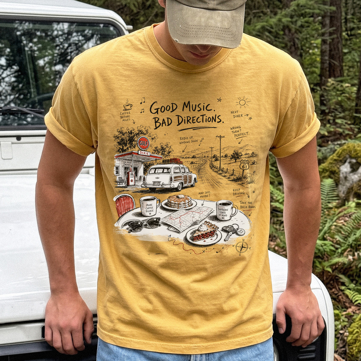 Man wearing a Mustard Comfort Colors T-shirt with a vintage roadside scene with a classic car, old gas station, and a winding back road