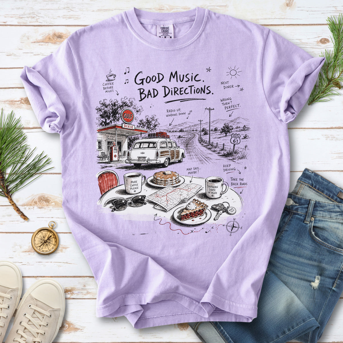 A vintage roadside scene with a classic car, old gas station, and a winding back road design on an Orchid Comfort Colors T-shirt