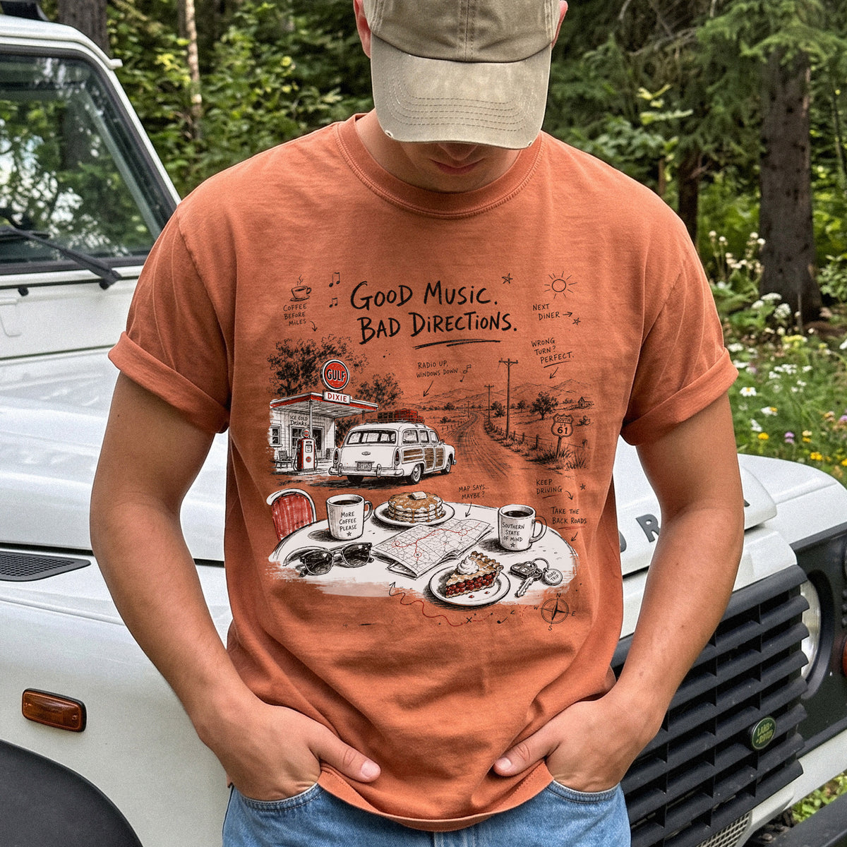 Man wearing a Yam Comfort Colors T-shirt with a vintage roadside scene with a classic car, old gas station, and a winding back road