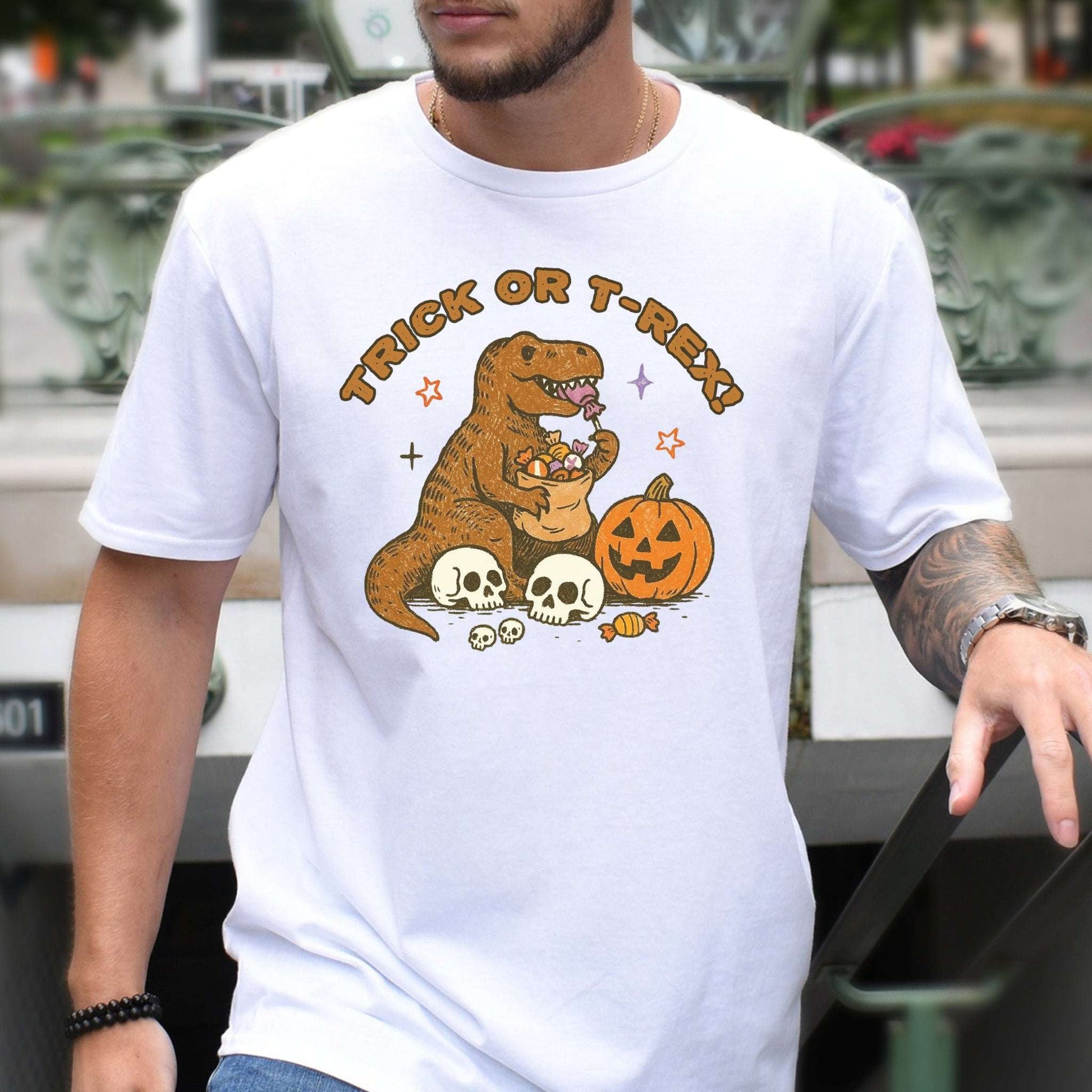 T-Rex Halloween T-Shirt featuring a dino with candy, skulls, and a pumpkin, perfect for Trick or Treat enthusiasts.