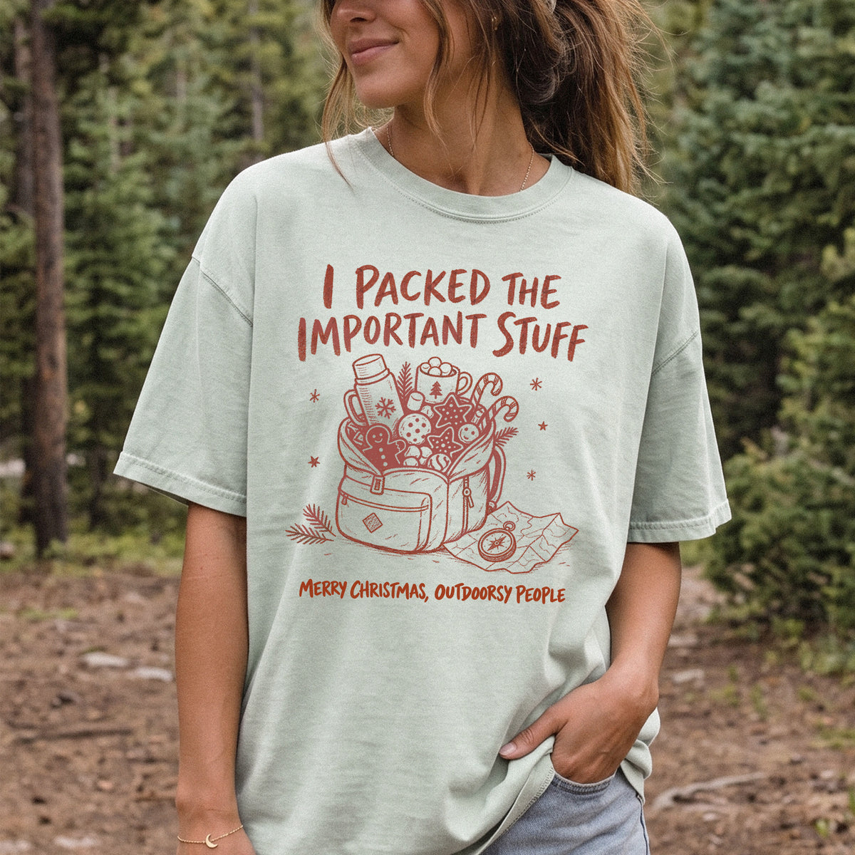 Woman wearing a Bay T-shirt printed with an overstuffed backpack with a thermos, mug, compass, trail map, and festive treats, doodle style