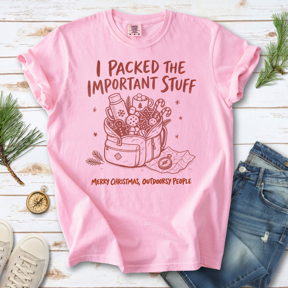 An overstuffed backpack with a thermos, mug, compass, trail map, and festive treats, doodle style design on a Blossom T-shirt
