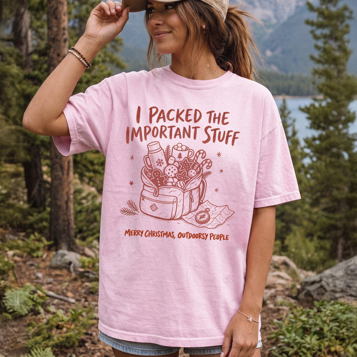 Woman wearing a Blossom T-shirt printed with an overstuffed backpack with a thermos, mug, compass, trail map, and festive treats, doodle style