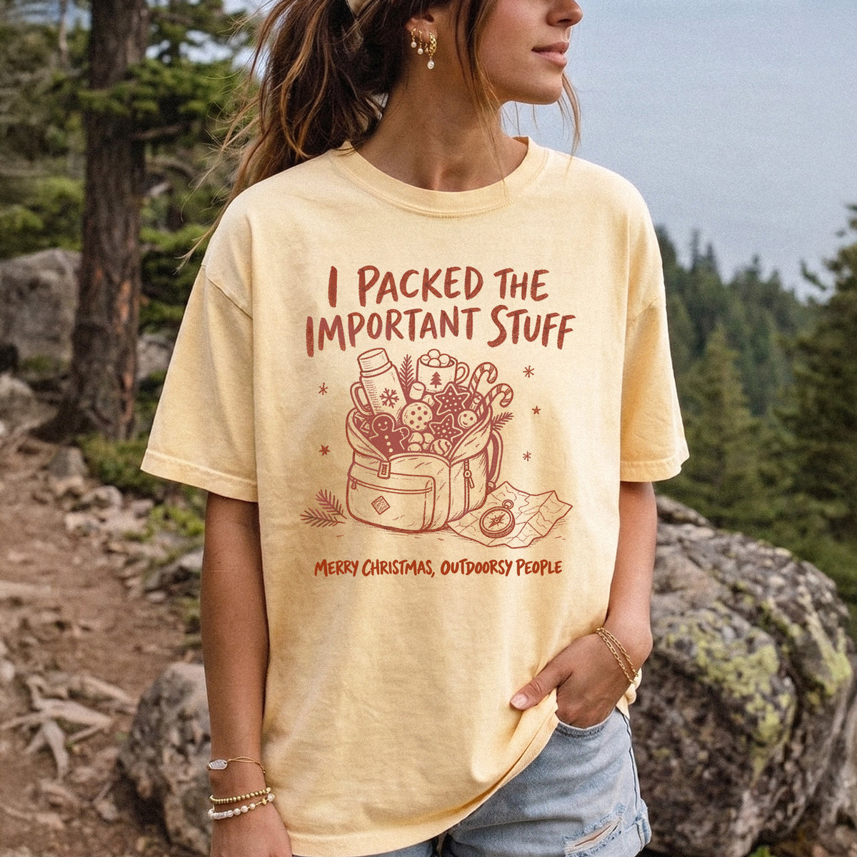 Woman wearing a Butter T-shirt printed with an overstuffed backpack with a thermos, mug, compass, trail map, and festive treats, doodle style