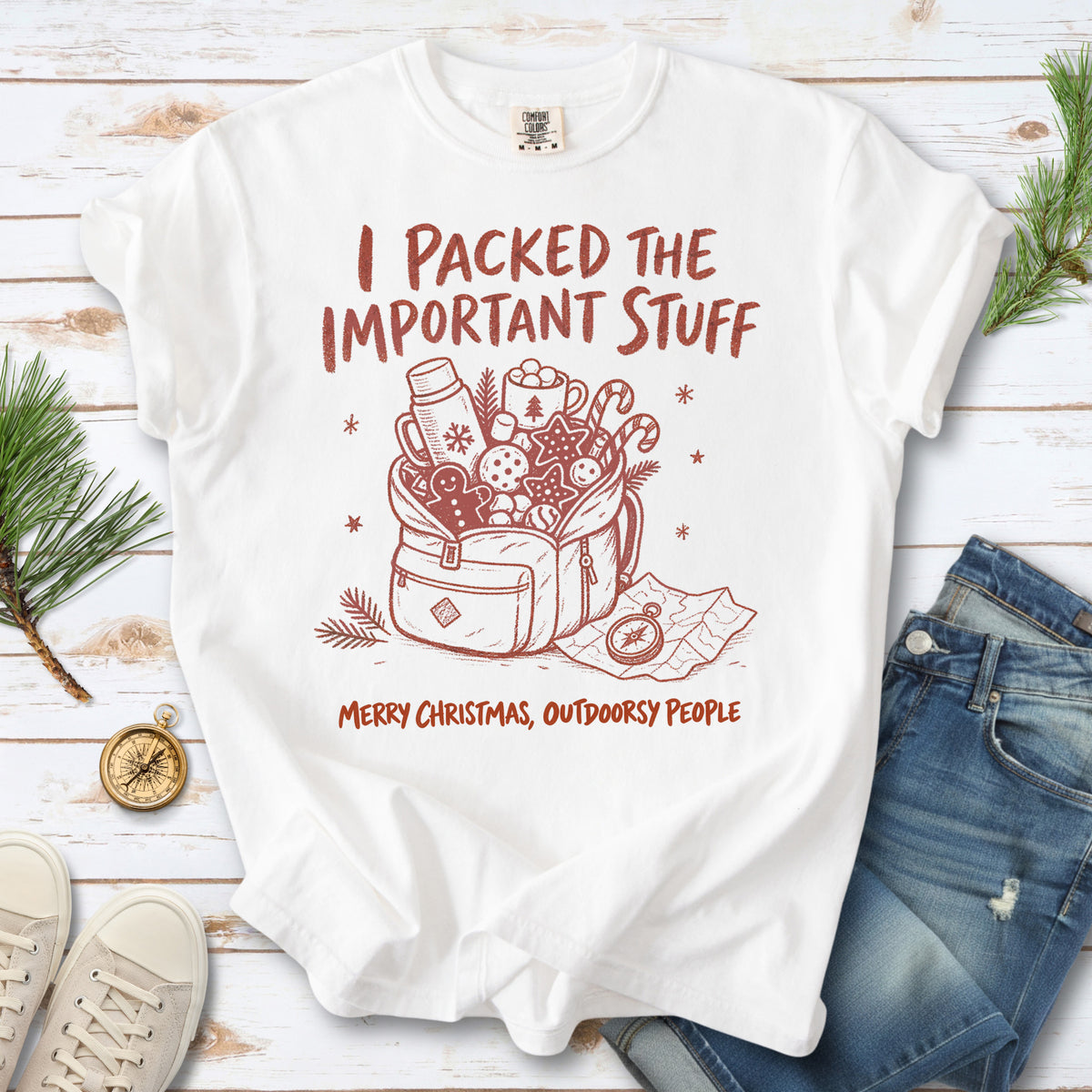 An overstuffed backpack with a thermos, mug, compass, trail map, and festive treats, doodle style design on a White T-shirt