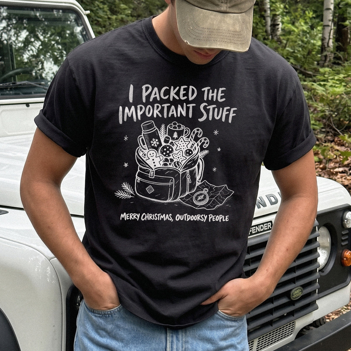 Man wearing a Black T-shirt printed with an overstuffed backpack with a thermos, mug, compass, trail map, and festive treats, doodle style