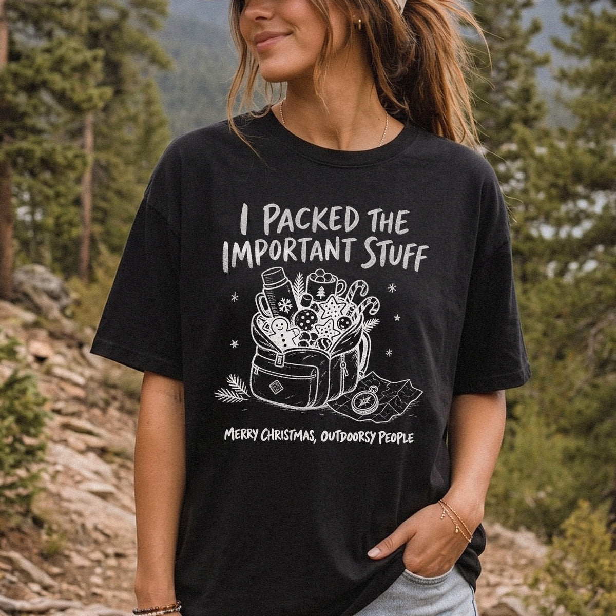 Woman wearing a Black T-shirt printed with an overstuffed backpack with a thermos, mug, compass, trail map, and festive treats, doodle style