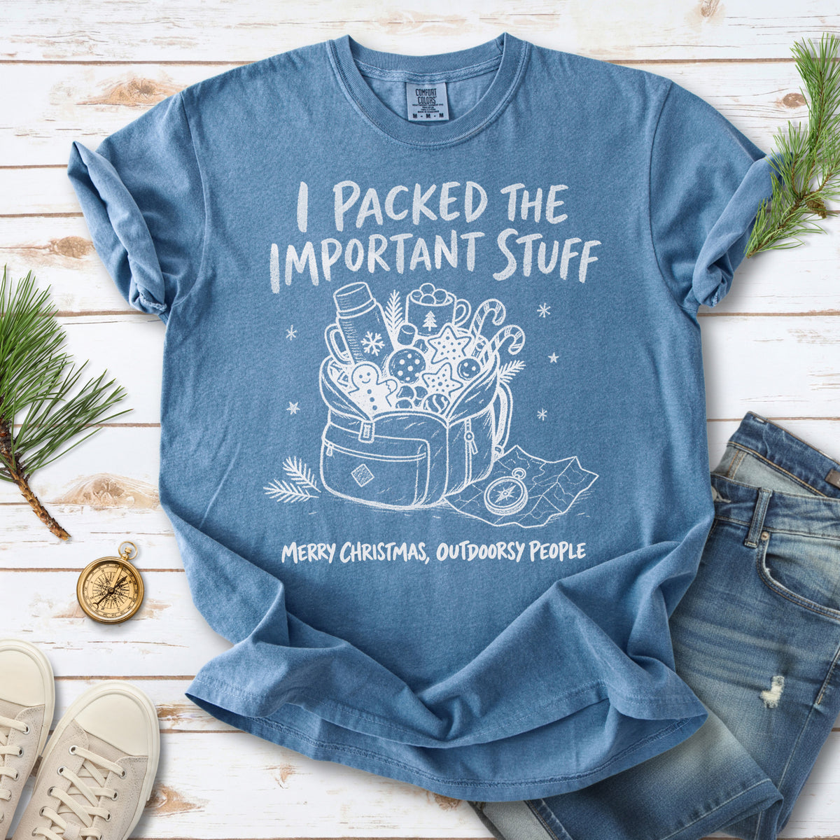 An overstuffed backpack with a thermos, mug, compass, trail map, and festive treats, doodle style design on a Blue Jean T-shirt