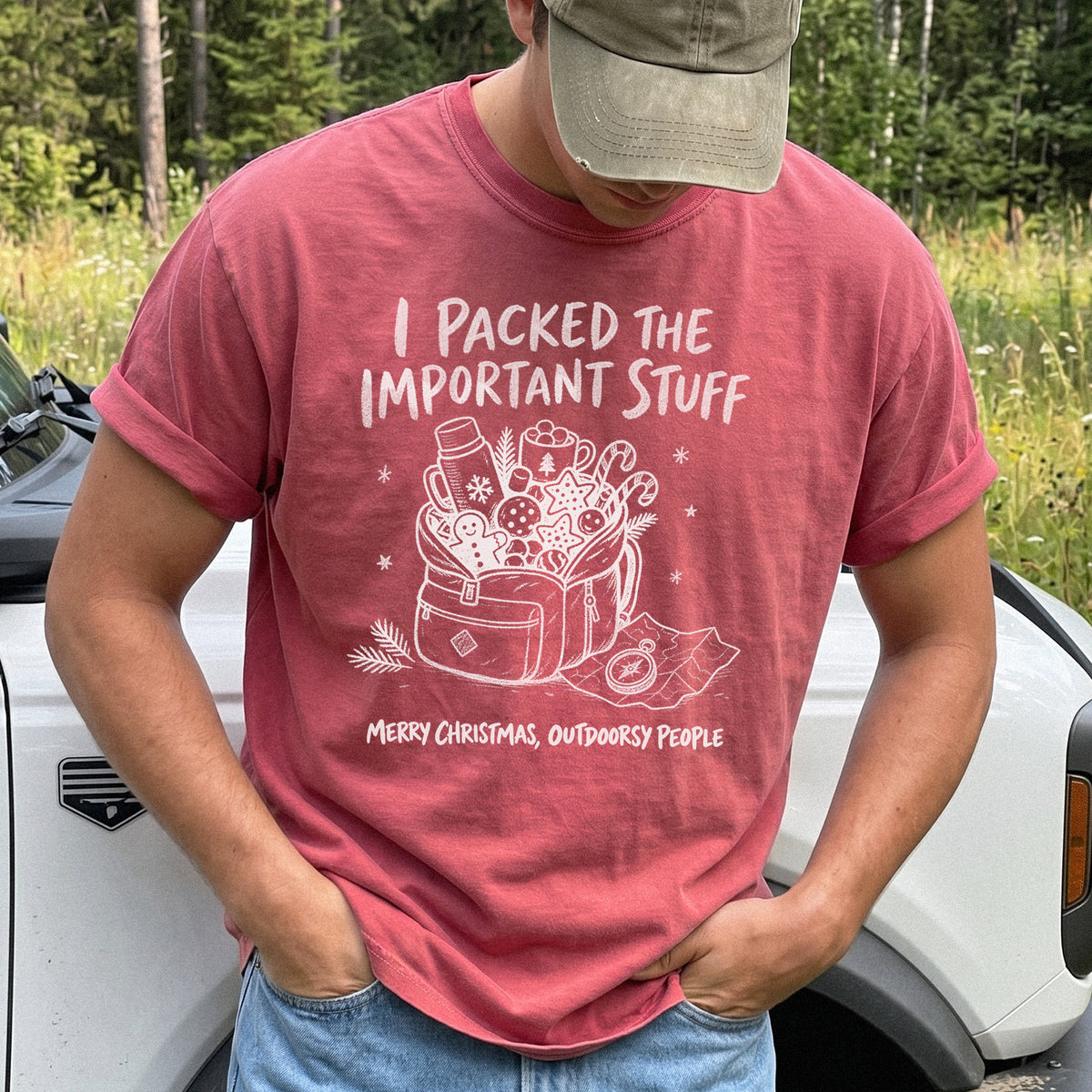 Man wearing a Crimson T-shirt printed with an overstuffed backpack with a thermos, mug, compass, trail map, and festive treats, doodle style