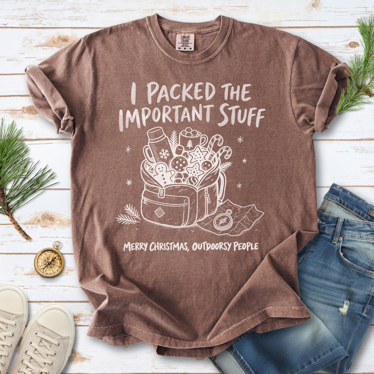 An overstuffed backpack with a thermos, mug, compass, trail map, and festive treats, doodle style design on an Espresso T-shirt