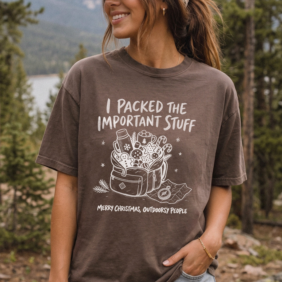 Woman wearing an Espresso T-shirt printed with an overstuffed backpack with a thermos, mug, compass, trail map, and festive treats, doodle style