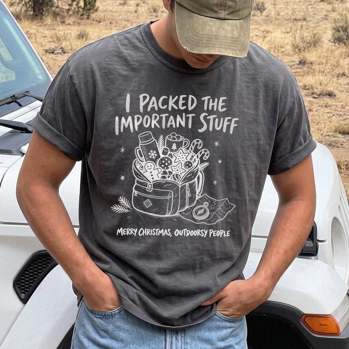 Man wearing a Pepper T-shirt printed with an overstuffed backpack with a thermos, mug, compass, trail map, and festive treats, doodle style