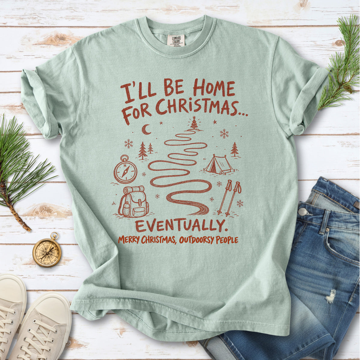 A winding trail with a tent, compass, backpack, trekking poles, snowflakes, and pine trees, doodle style design on a Bay T-shirt