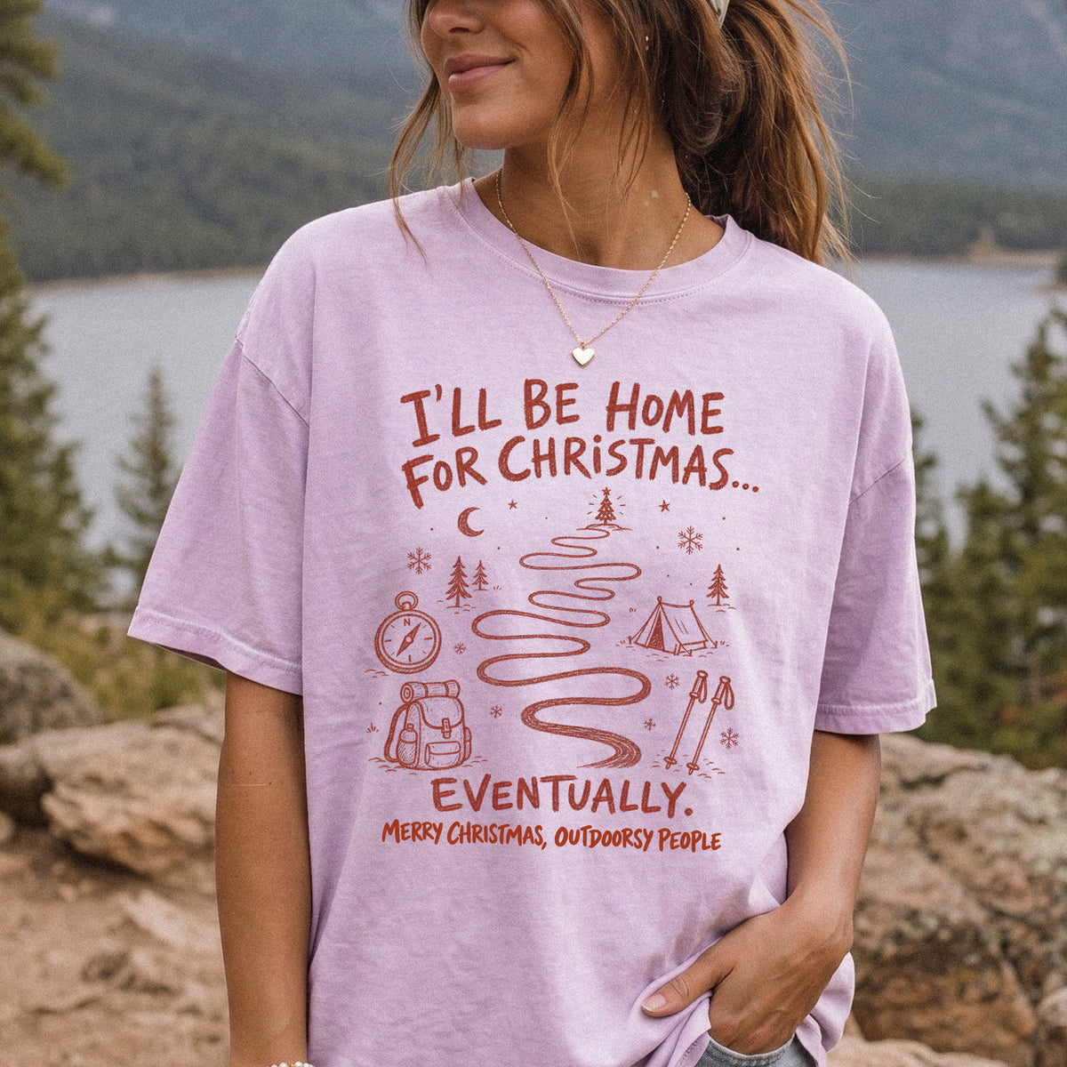 Woman wearing an Orchid T-shirt printed with a winding trail with a tent, compass, backpack, trekking poles, snowflakes, and pine trees, doodle style